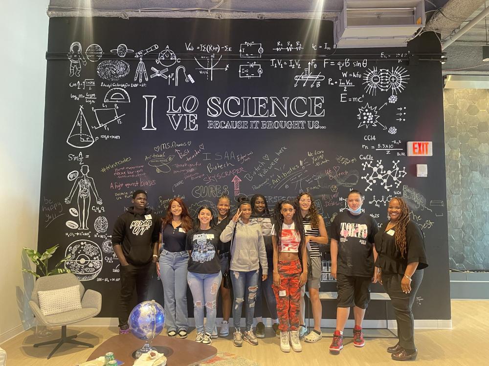 A group of teenagers and adults standing in front of a wall with the message : I love science because it brought us... 
